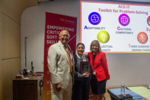 Three individuals smiling and standing together, with the person in the center holding an award plaque. 